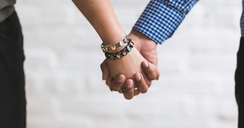 Erstes Date Tipps: Paar hält sich vor einer weissen Wand an den Händen